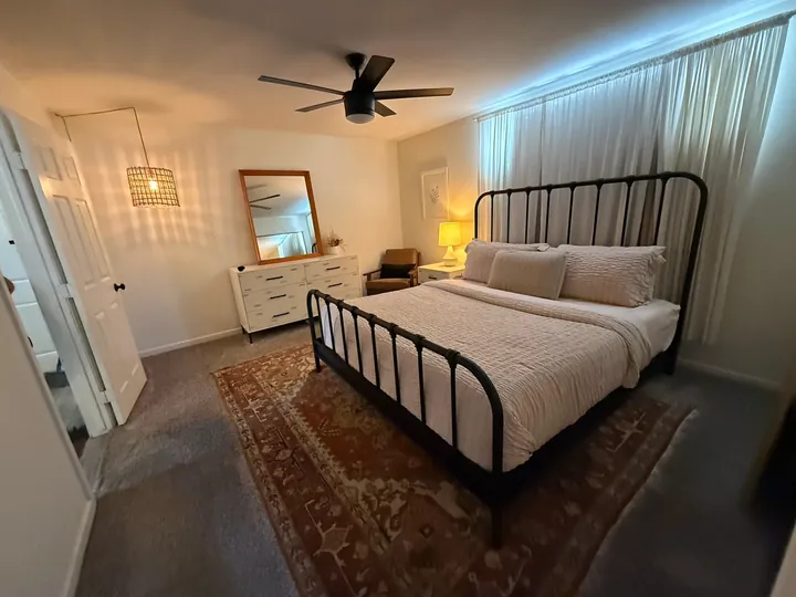 Bedroom with a black iron bed, cream bedding and a patterned rug after a Greater Phoenix Cleaning deep clean