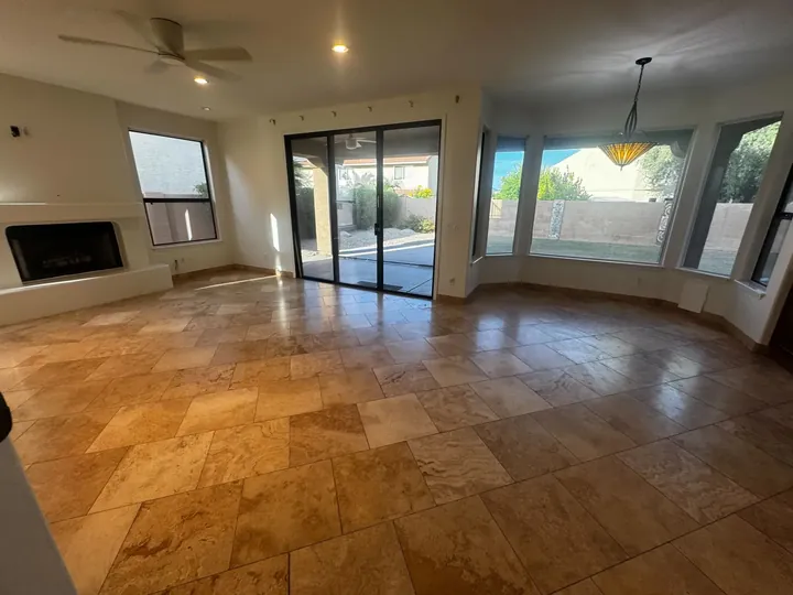 Empty great room with travertine floors, a fireplace and patio doors in a home Greater Phoenix Cleaning cleaned