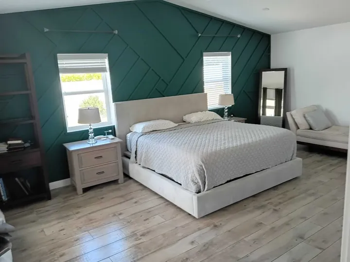 Bedroom with a green geometric accent wall, an upholstered bed and light wood floors in a home Greater Phoenix Cleaning cleaned